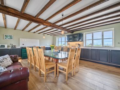 A kitchen dining room with wooden chairs around a table a brown leather sofa and wooden ceiling beams at The Chestnuts in Tenbury Wells