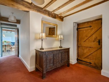 A hallway with wooden beams a wooden door a carved wooden chest with two lamps and a mirror above at The Chestnuts in Tenbury Wells