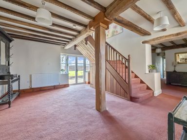 A room with wooden ceiling beams pink carpet and a wooden staircase at The Chestnuts in Tenbury Wells