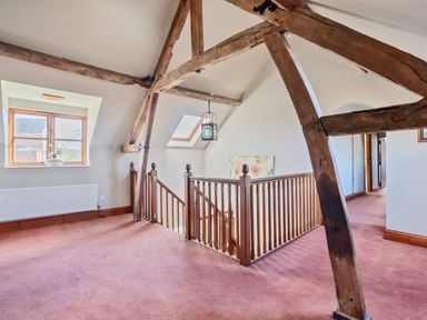 A landing area with wooden beams and bannisters and pink carpet flooring at The Chestnuts in Tenbury Wells