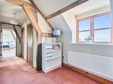A hallway with exposed wooden beams a white bookshelf with books a table lamp and a window with flowers at The Chestnuts in Tenbury Wells
