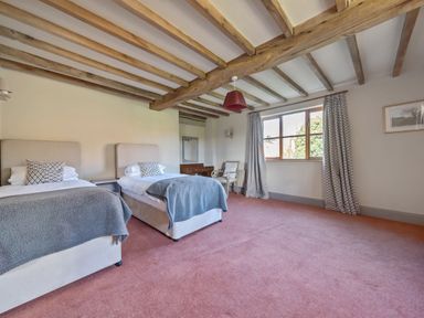 A bedroom with two single beds a window with patterned curtains and wooden ceiling beams at The Chestnuts in Tenbury Wells