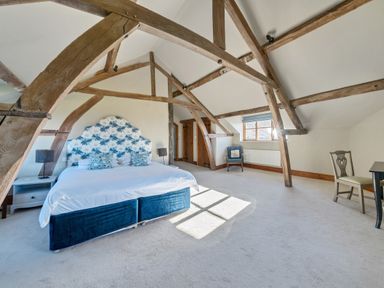 A bedroom with a double bed blue upholstered base and floral headboard wooden beams a window two chairs and a desk at The Chestnuts in Tenbury Wells