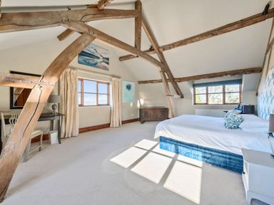 A bedroom with wooden beams two windows a bed with blue and white bedding a desk with a chair and a lamp and a wooden chest at The Chestnuts in Tenbury Wells