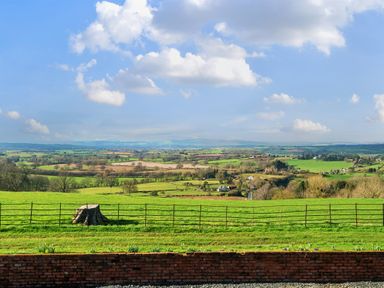 A rural landscape with green fields and a tree stump behind a metal fence at The Chestnuts in Tenbury Wells