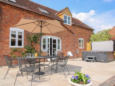 An outdoor patio with a metal table and chairs under an umbrella next to a hot tub at The Chestnuts in Tenbury Wells