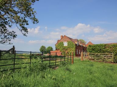 A brick house with ivy on the walls behind metal and wooden gates in a grassy field at The Chestnuts in Tenbury Wells