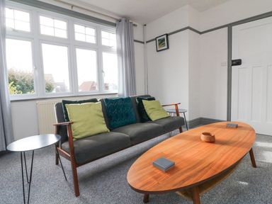 A living room with a gray sofa with green and blue cushions a wooden coffee table and side tables at Chilton in Bude
