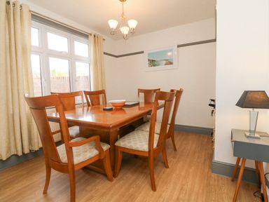 A dining room with a wooden table and six chairs a side table with a lamp and a framed picture on the wall at Chilton in Bude