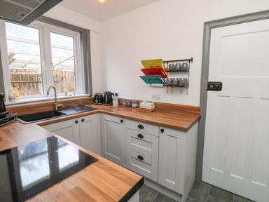 A kitchen with wooden countertops gray cabinets a black sink stove and wall-mounted racks at Chilton in Bude