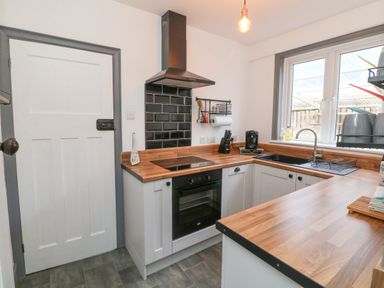 A kitchen with wooden countertops a black oven and stovetop a white door a window and a sink at Chilton in Bude
