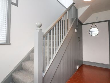 A staircase with gray railing and carpeted steps next to a hallway with red tiled floor and round mirror on the wall at Chilton in Bude
