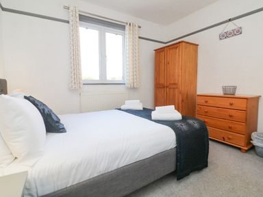 A bedroom with a bed and folded towels on top a wooden wardrobe and a chest of drawers under a window at Chilton in Bude
