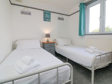 A bedroom with two single beds white bedding bedside table with lamp and window with teal curtains at Chilton in Bude