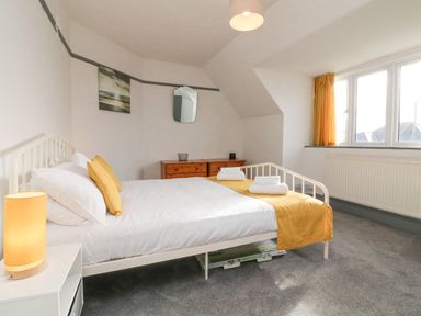 A bedroom with a bed with yellow pillows and runner a bedside table with a lamp a chest of drawers and a window with yellow curtains at Chilton in Bude