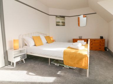 A bedroom with a white metal bed frame yellow pillows and blanket a white nightstand with a lamp wooden dresser with a mirror and carpeted floor at Chilton in Bude