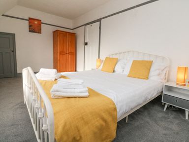 A bedroom with a white metal bed frame yellow pillows and runner wooden wardrobe and bedside tables with lamps at Chilton in Bude