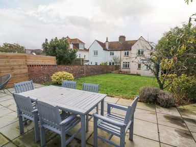 A patio with a table and chairs next to a grass lawn and a white house in the background at Chilton in Bude