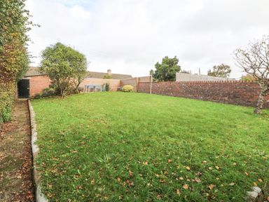 A backyard with green grass trees and a table with chairs against a wooden fence at Chilton in Bude