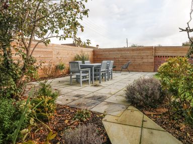A patio area with a table and six chairs surrounded by plants and wooden fencing at Chilton in Bude