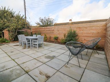 An outdoor patio area with a dining table and six chairs and two round lounge chairs surrounded by a wooden fence at Chilton in Bude