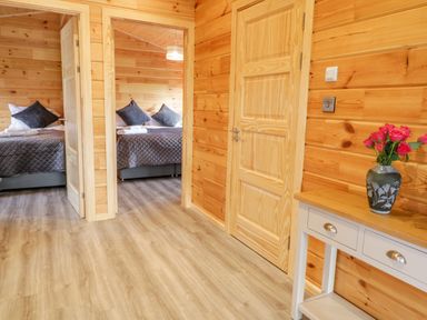 A wooden hallway with a table holding a vase of flowers and a view into a bedroom with a bed at Bryn Eiddon Log Cabin in Machynlleth