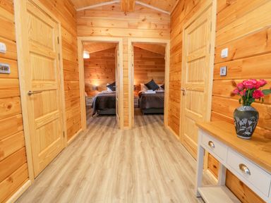 A wooden hallway with doors leading to two bedrooms and a table with a vase of flowers at Bryn Eiddon Log Cabin in Machynlleth