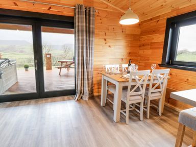 A dining area with a table set for four near large glass doors and wooden walls at Bryn Eiddon Log Cabin Machynlleth