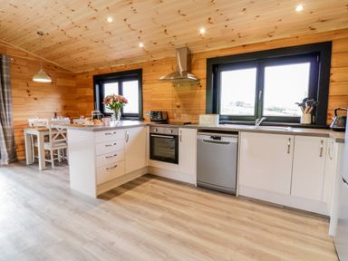 A kitchen with white cabinets and dining table with flowers at Bryn Eiddon Log Cabin in Machynlleth