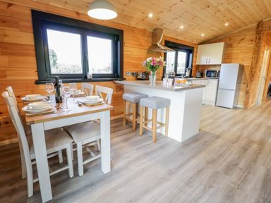 A kitchen and dining area with a table set for four and a kitchen island with stools at Bryn Eiddon Log Cabin in Machynlleth