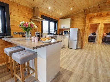A kitchen area with a breakfast bar with two stools flowers croissants and coffee at Bryn Eiddon Log Cabin in Machynlleth