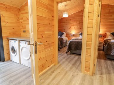 A laundry area with a washing machine and dryer next to a bedroom with two beds and bedside tables at Bryn Eiddon Log Cabin in Machynlleth