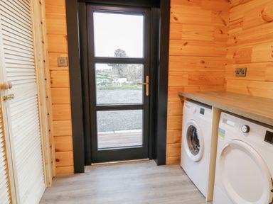 A utility room with a washing machine and dryer under a wooden countertop by a glass door at Bryn Eiddon Log Cabin in Machynlleth