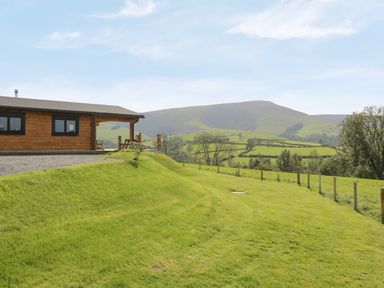 A grassy landscape with a wooden cabin and hills in the background at Bryn Eiddon Log Cabin in Machynlleth