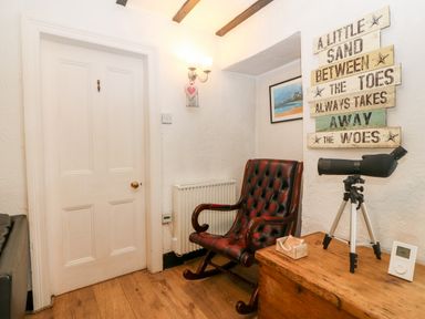 A room with a wooden rocking chair a telescope on a wooden chest and a sign on the wall at Tyddyn Serri in Rhosneigr