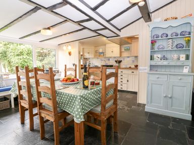 A dining area with wooden chairs around a table with a polka dot tablecloth and a blue cabinet with blue and white crockery at Tyddyn Serri in Rhosneigr