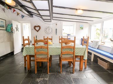 A dining area with a wooden table and chairs with a green polka dot tablecloth and a window seat with cushions at Tyddyn Serri in Rhosneigr