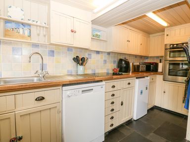 A kitchen with beige cabinets dishwasher small fridge and oven at Tyddyn Serri in Rhosneigr