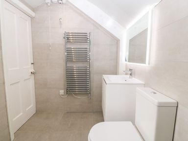 A bathroom with a white door a chrome towel radiator a white sink cabinet a mirror above the sink and a white toilet at Tyddyn Serri in Rhosneigr