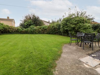 A backyard with green grass and a patio area with a metal table and chairs at Tyddyn Serri in Rhosneigr