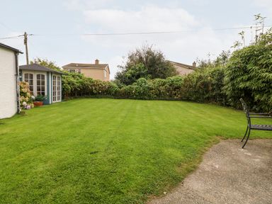 A garden with a green lawn a small shed and a metal chair at Tyddyn Serri in Rhosneigr