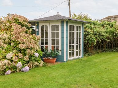A small garden shed with glass windows and doors next to flowering bushes on a lawn at Tyddyn Serri in Rhosneigr