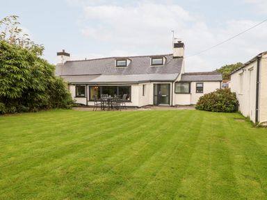 A back view of a house with a green lawn and outdoor table with chairs at Tyddyn Serri in Rhosneigr