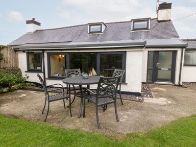 A small patio area with a round metal table and four chairs outside a white house with two dormer windows at Tyddyn Serri in Rhosneigr