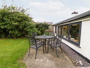 An outdoor patio area with a round metal table and four chairs next to a white building at Tyddyn Serri in Rhosneigr