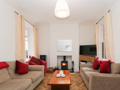 A living room with two beige sofas red cushions a red armchair a wooden coffee table a wood stove and a television at Beach House in Bridlington