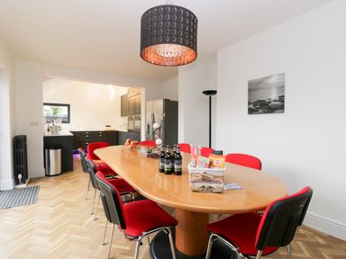 A dining room with a wooden table and red chairs next to a kitchen in a Beach House in Bridlington