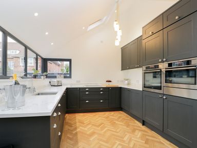 A kitchen with dark cabinets white countertops built in ovens and wooden parquet floor at Beach House in Bridlington