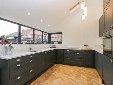 A kitchen with dark cabinets white countertops wooden floor and large windows at Beach House in Bridlington
