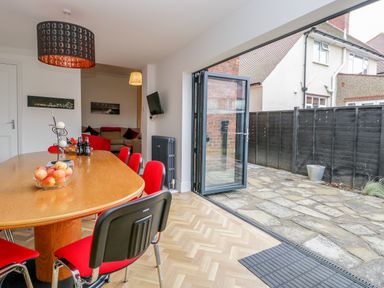 A dining area with a wooden table and red chairs next to an open folding door leading to a stone patio at Beach House in Bridlington